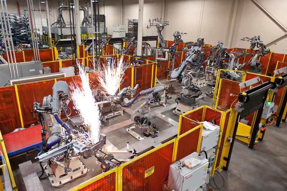 Multi-robot welding cell in production, sparks flying during an automated weld cycle